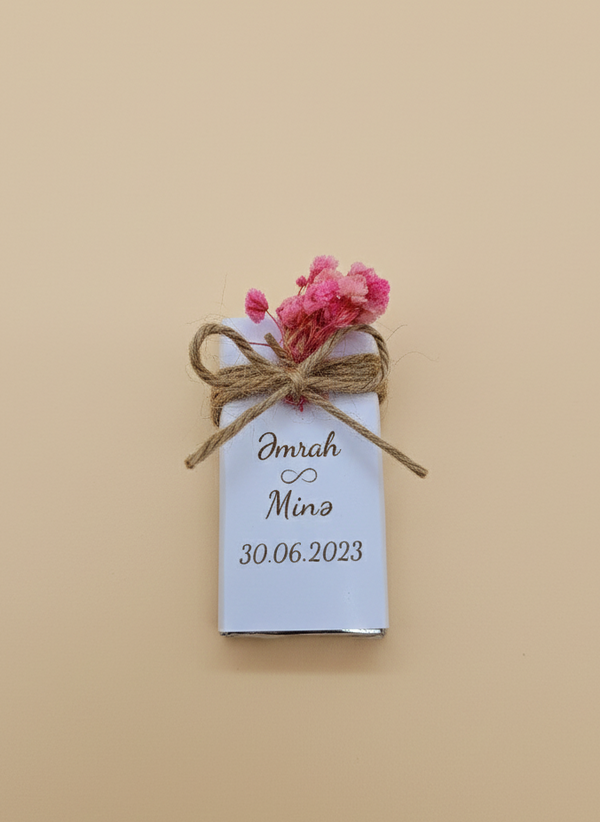 Small wrapped chocolate gift with a tag and pink flowers on a beige background