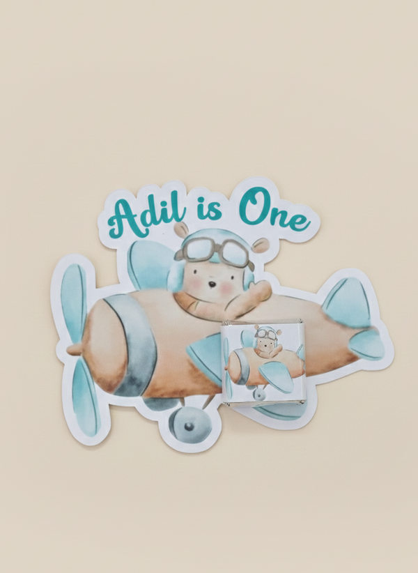 Sticker of a bear in an airplane with 'Adil is One' text on a beige background