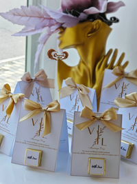 Decorative boxes with gold ribbons and a blurred background of a person wearing a yellow dress and pink headband.