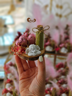 Hand holding a small decorative item with flowers and a heart-shaped object.