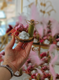Hand holding a small decorative item with blurred floral background