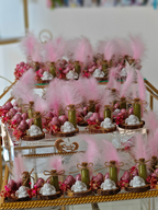 Decorative dessert table with pink feathers and various treats on a gold stand.