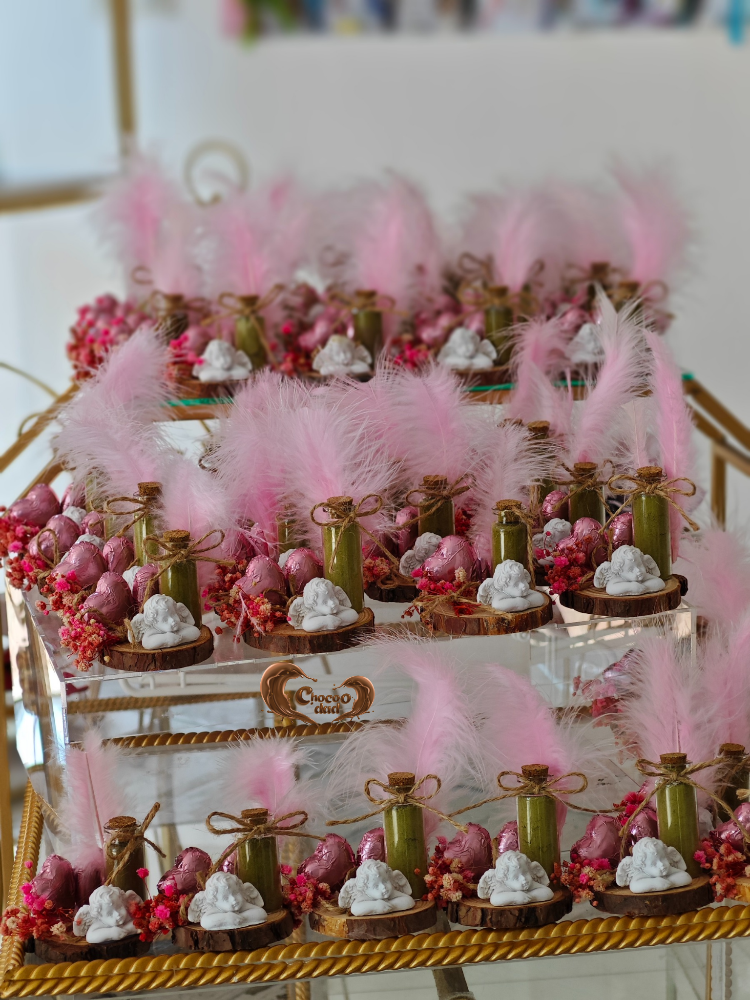 Decorative dessert table with pink feathers and various treats on a gold stand.