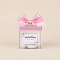Drajee chocolate in a transparent box with a pink bow and personalized label on a beige background