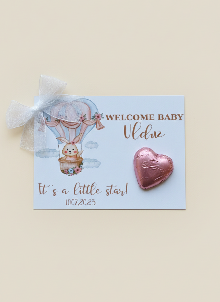 Heart-shaped pink baby shower favor with a card featuring a hot air balloon and baby bear design on a beige background.