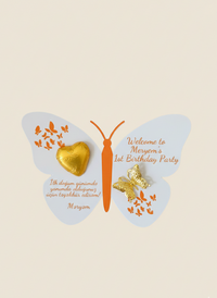 Butterfly-shaped party favor with gold heart, wings, and text on a beige background