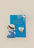 Children's party favor with a boy in overalls and hat and a heart-shaped object on a blue card.