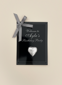 Black birthday party invitation with silver heart and bow on a beige background