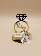 Decorative cake topper with 'R&A' on a beige background and chocolate, engagement chocolate favours