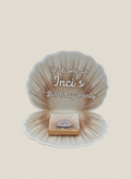 Seashell-shaped party favor with 'Welcome to Inci's 1st Birthday Party' text on a beige background
