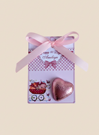 Pink heart-shaped gift with ribbon and decorative card on a beige background