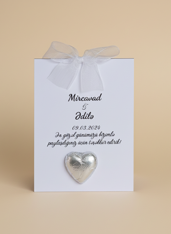 Heart-shaped silver pin on a white card with text, tied with a ribbon on a beige background