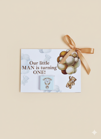 Gift with balloons and teddy bear on a card, featuring text 'Our little MAN is turning ONE!' against a beige background.