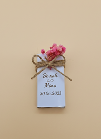 Small wrapped chocolate gift with a tag and pink flowers on a beige background