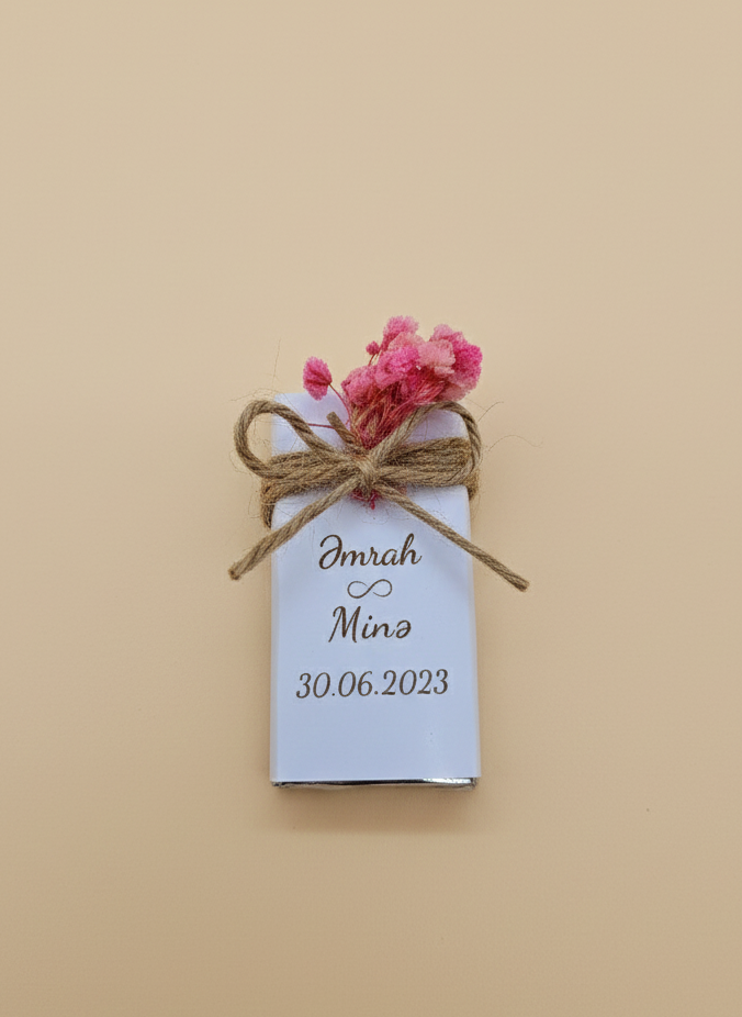 Small wrapped chocolate gift with a tag and pink flowers on a beige background