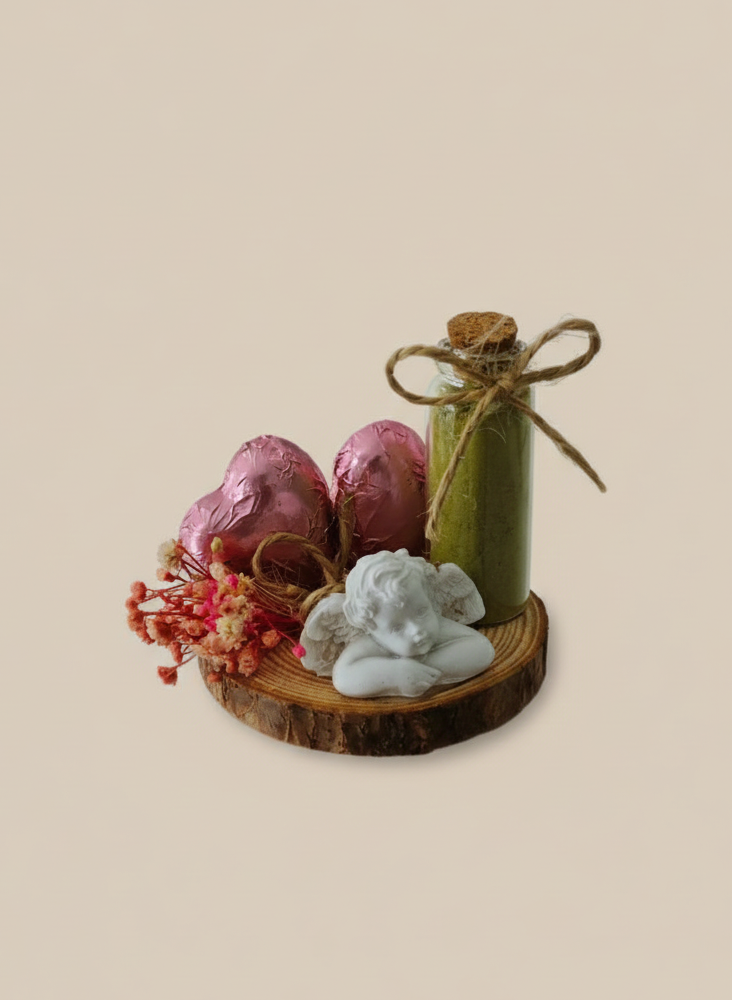 Decorative arrangement with a green candle, pink eggs, and a white figurine on a wooden base against a beige background.