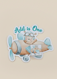 Sticker of a bear in an airplane with 'Adil is One' text on a beige background