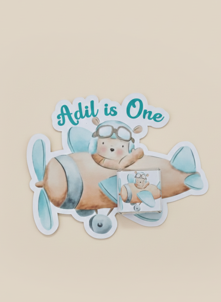 Sticker of a bear in an airplane with 'Adil is One' text on a beige background