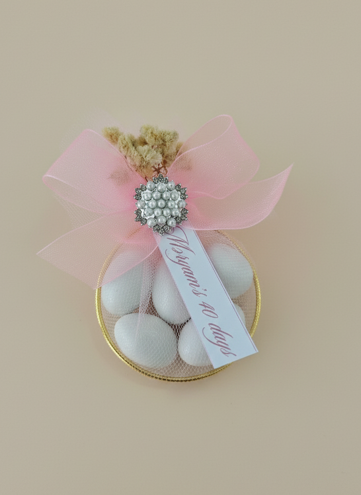 Decorative gift with pink ribbon, white candies, and a decorative tag on a beige background