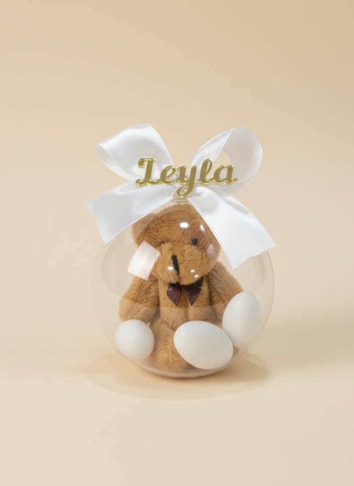 Teddy bear in a clear ball with a white ribbon and 'Leyla' text on a beige background