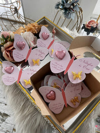 Butterfly-shaped cards with pink hearts and gold butterflies in a box, surrounded by flowers.