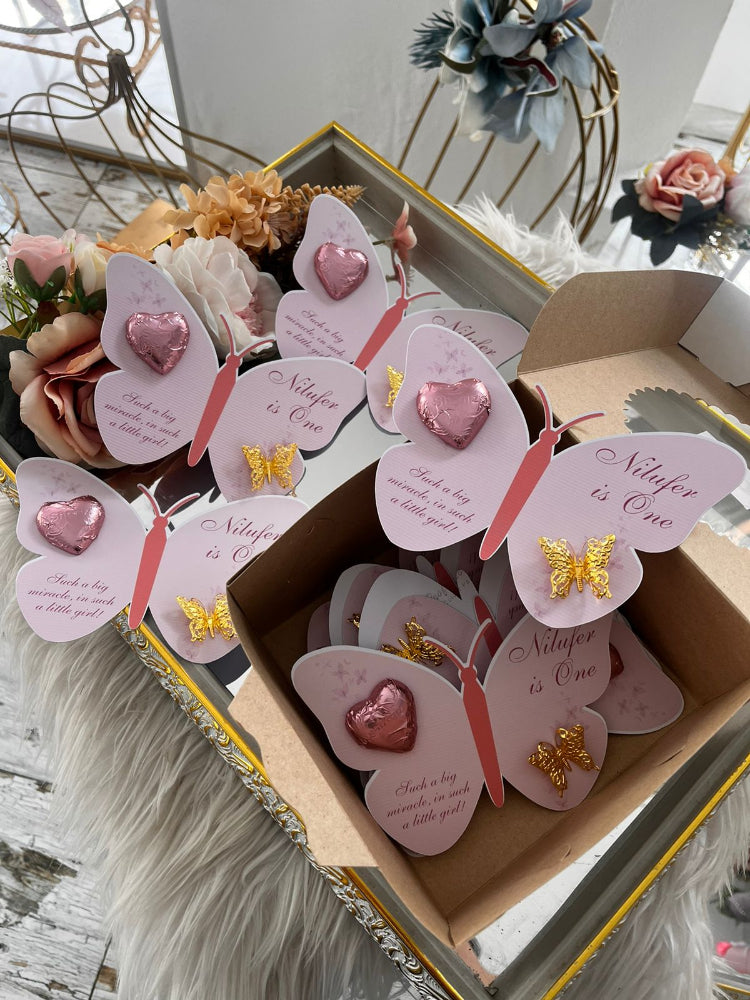 Butterfly-shaped cards with pink hearts and gold butterflies in a box, surrounded by flowers.