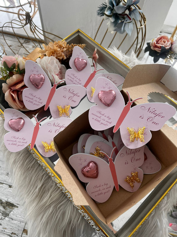 Butterfly-shaped cards with pink hearts and gold butterflies in a box, surrounded by flowers.