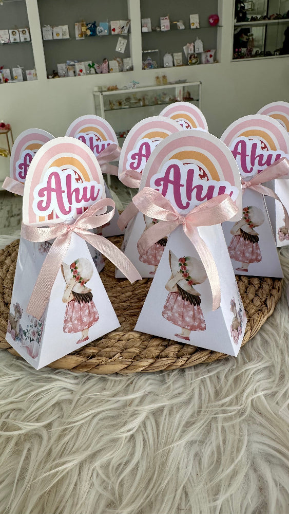 Triangular favor boxes with 'Ahu' text and pink ribbons on a textured surface.