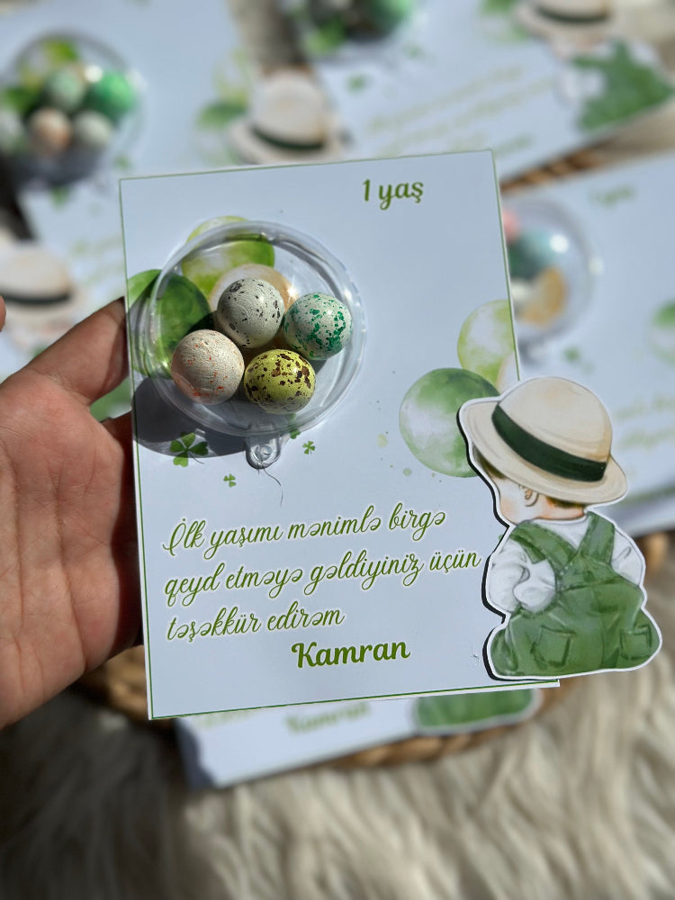Hand holding a small card with a design of eggs and a person wearing a hat, on a blurred background.