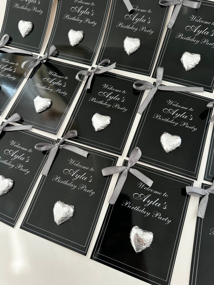 Black favor boxes with silver ribbons and decorative stones on a white surface