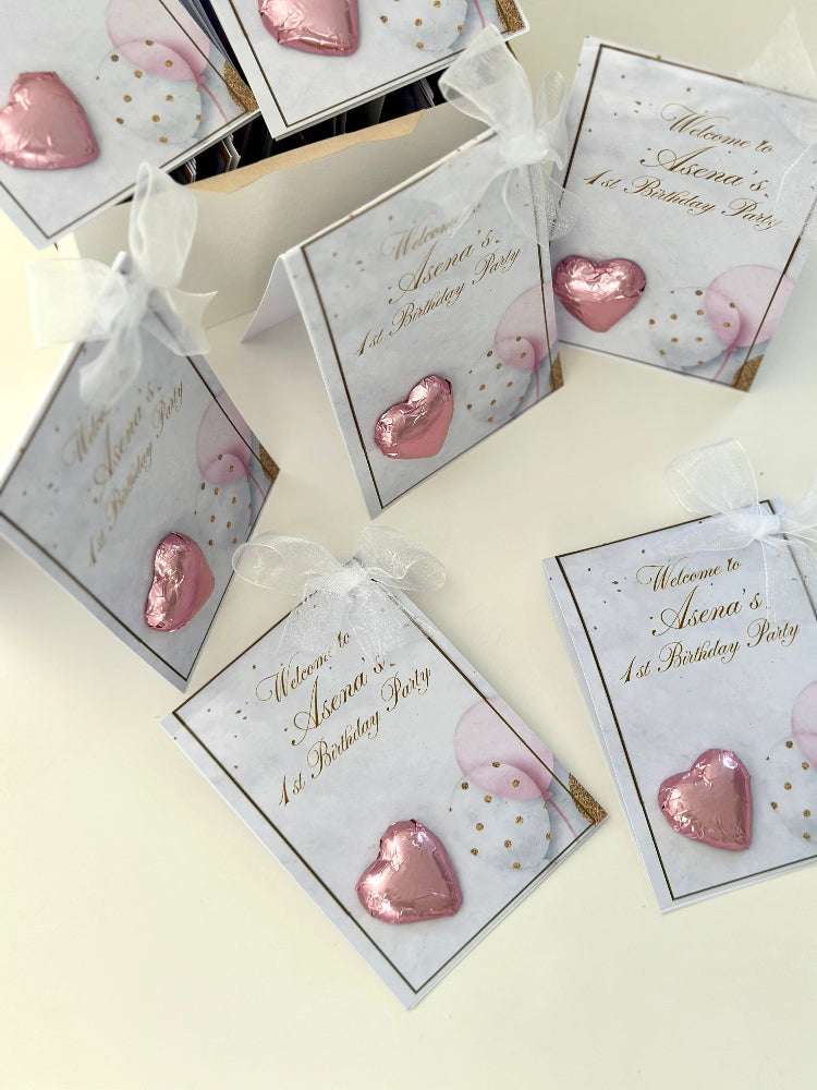 Pink heart-shaped favors with birthday party cards on a light background