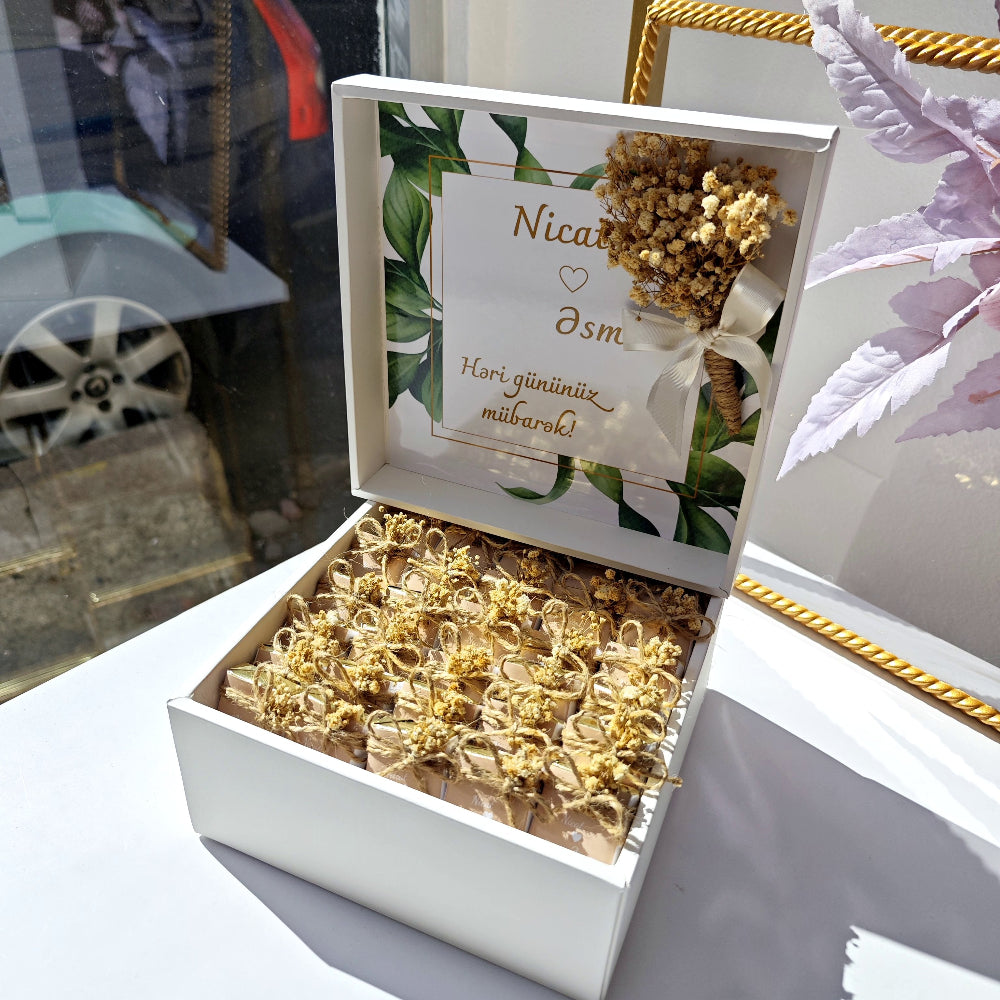 Decorative box with gold bow decorations and a card inside, on a table.