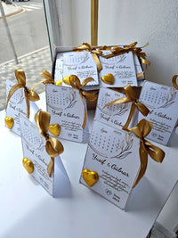 Small boxes with gold ribbons and personalized labels on a white surface.