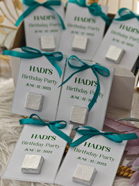 Silver favors with teal ribbons on personalized cards for Hadi's Birthday Party.