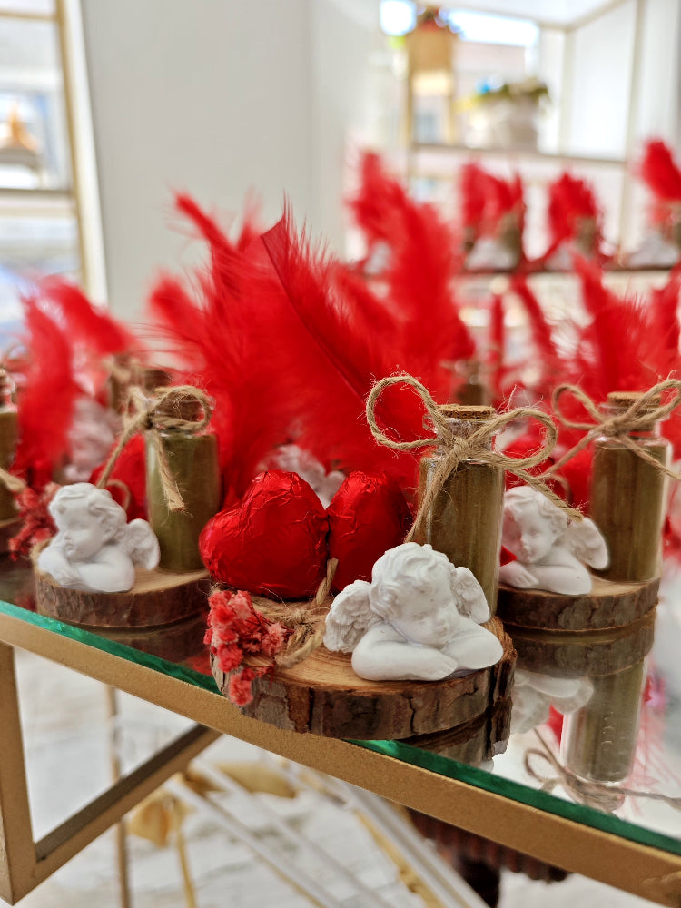 Decorative setup with red feathers, wooden vases, and white sculptures on a glass table.