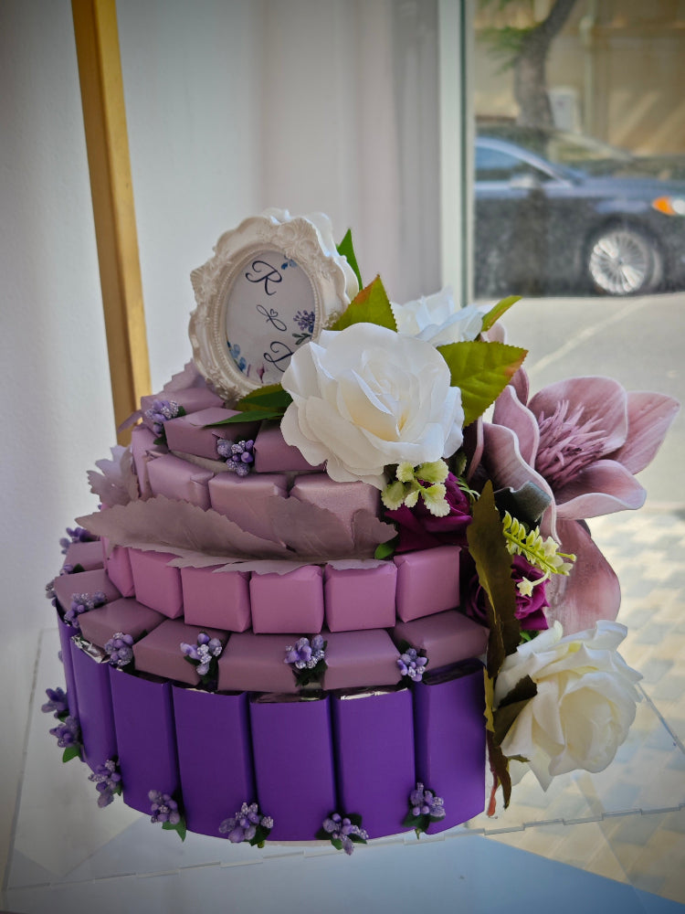 Three-tiered purple chocolate arrangement with floral decorations on a white surface.