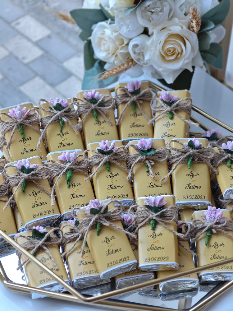 Decorative boxes with personalized labels on a reflective surface with flowers in the background