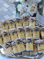 Decorative boxes with personalized labels on a reflective surface with flowers in the background