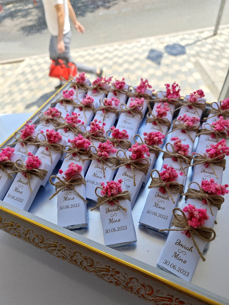 Decorative boxes with pink flowers and personalized labels on a reflective surface.