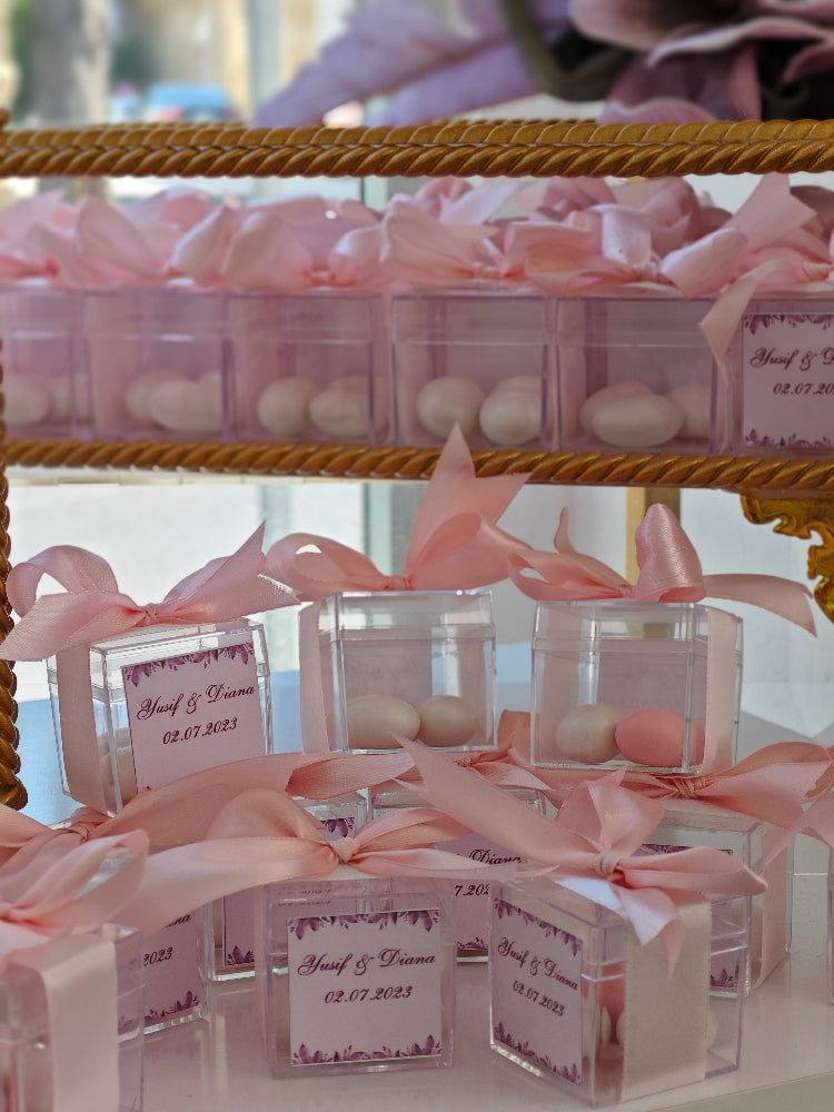 Clear containers with pink ribbons and labels on a gold stand.
