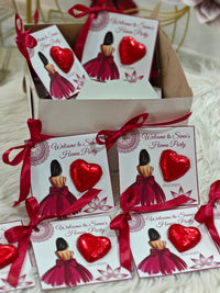 Red heart-shaped favors with matching ribbons and 'Welcome to Sina's Home Party' cards on a white surface.