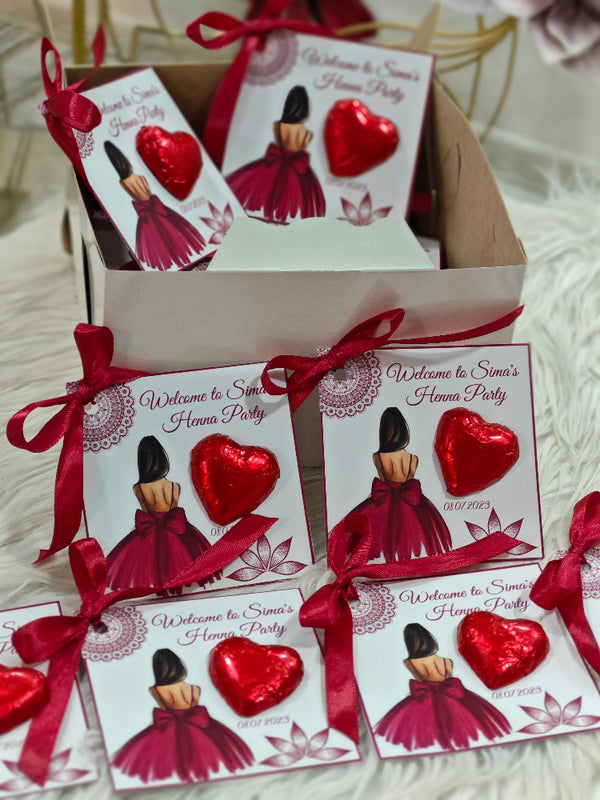 Red heart-shaped favors with matching ribbons and 'Welcome to Sina's Home Party' cards on a white surface.