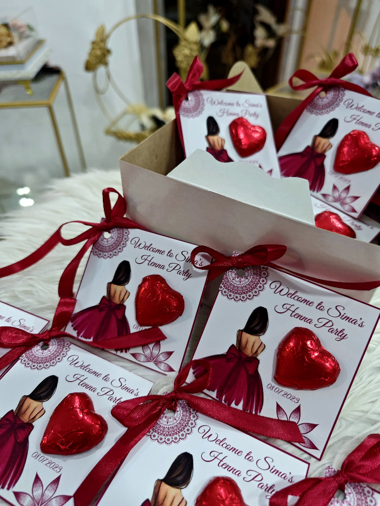 Henna party invitations with red ribbons and heart-shaped decorations on a white surface.