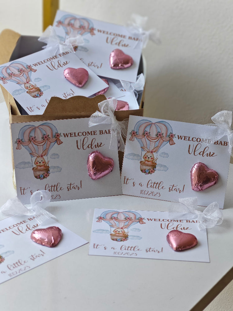 Pink heart-shaped balloons with 'Welcome Baby' cards on a white surface