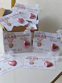 Pink heart-shaped balloons with 'Welcome Baby' cards on a white surface