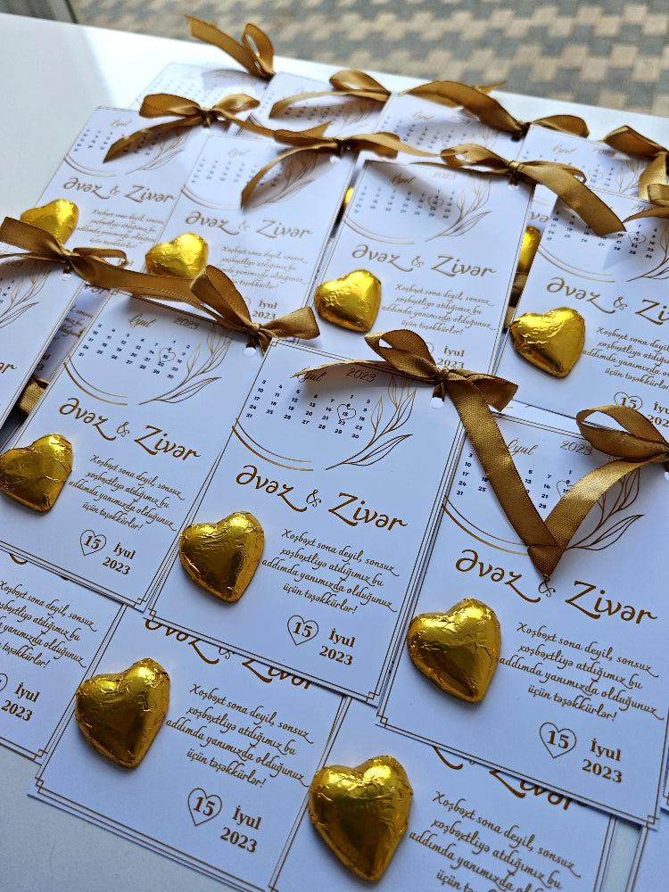 Wedding invitations with gold ribbons and heart-shaped decorations on a white surface.