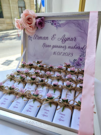 Decorative box with floral elements and personalized names on a blurred outdoor background