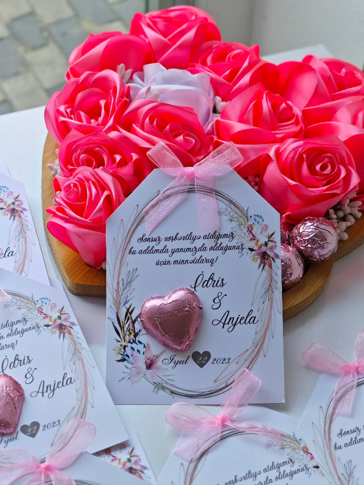 Heart-shaped arrangement of pink soap flowers with a card in the center on a white surface.