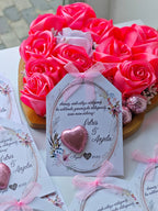 Heart-shaped arrangement of pink soap flowers with a card in the center on a white surface.