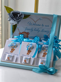 Baby shower gift set with teddy bear design and blue ribbons on a white surface.